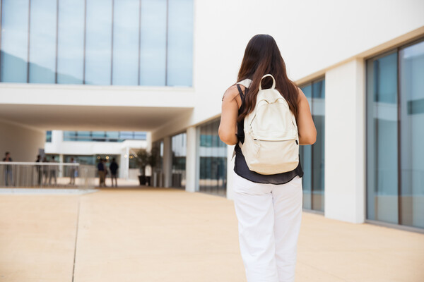 A person wearing a backpack outside a university building.