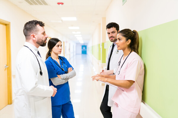 Four doctors and nurses having a discussion in a hospital hallway.