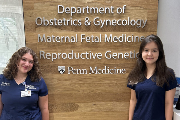 Ellie Mayers and Gladys Smith in front of a sign reading Department of Obstetrics & Gynecology Maternal Fetal Medicine Reproductive Genetics at Penn Medicine.