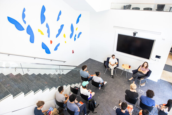 A stairwell and mural next to a group of students sitting in chairs.