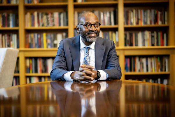 John Jackson rests his hands on a table in front of a bookcase.