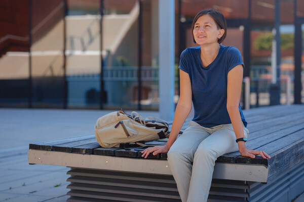 A college student sitting on a bench outside a university building.