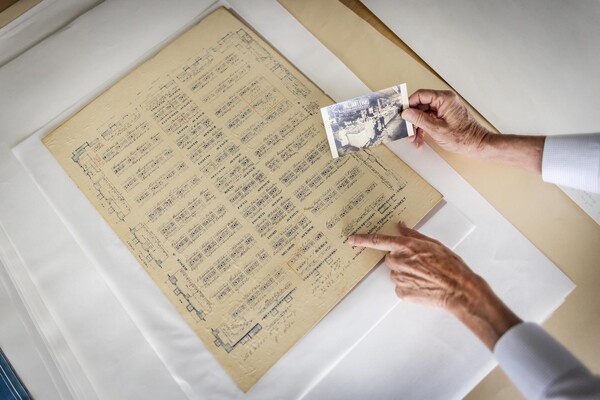 yellowed historic document with a grid of squares and a hand holding a photo