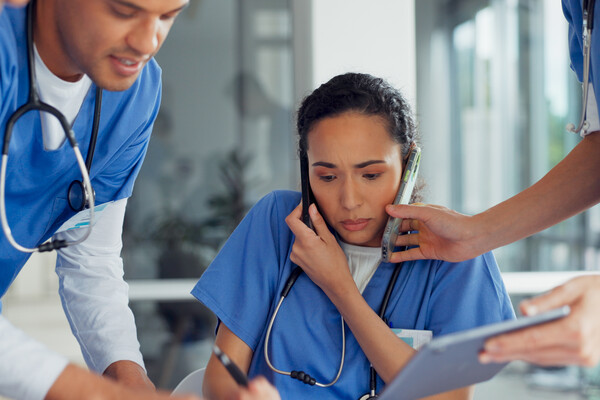 Three nurses with smartphones and charts looking overworked.