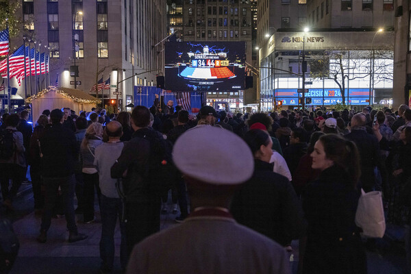 A group of people, seen from behind, watch election results from NBC News on a livestream display at Rockefeller Center in New York City.