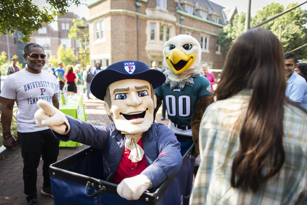 The Philly Eagles mascot pushing the Penn Quaker mascot in a Move-In cart on Penn’s campus.