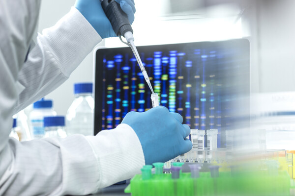 A scientist with a pipette and a test tube with a computer screen in the background.