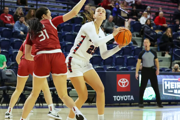 Katie Collins makes a move with the ball while guarded by two defenders.