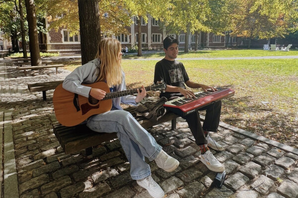 Grace Gramins plays a guitar with a friend on keyboard on Penn’s campus.