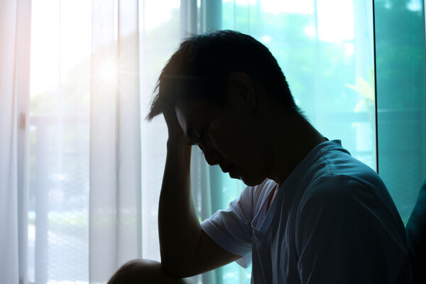 A person holding their head in pain near a window.