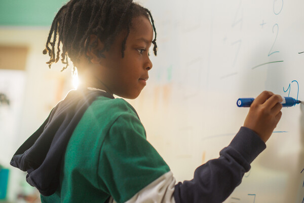 A young student writing a math equation on a white board.