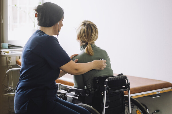 A nurse checks the heartbeat of a patient in a wheelchair.