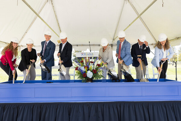 Eight people on stage with shovels for ceremonial groundbreaking.