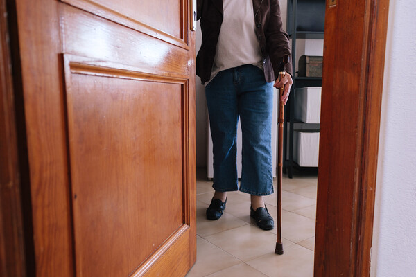 An elderly person opening a door with a cane in hand.