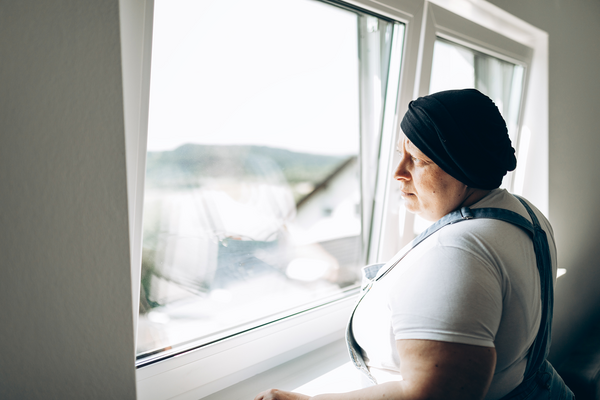 Person with head covering looking out a window.