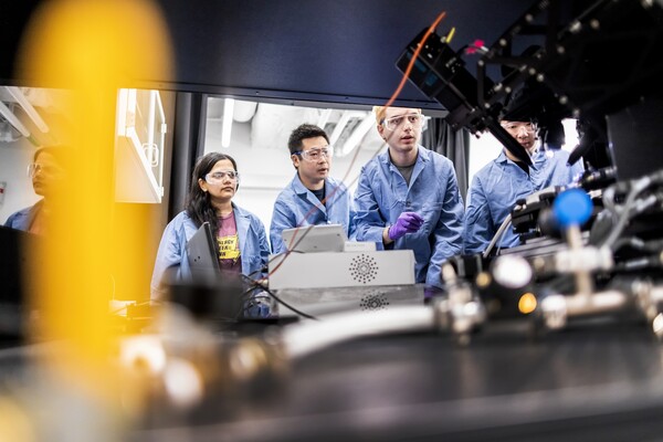 Researchers stand next to s microscope.