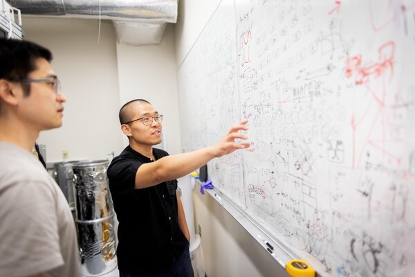 Researchers stand and point at a white board littered with equations.