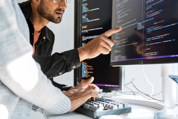 Two people work on coding at computer.
