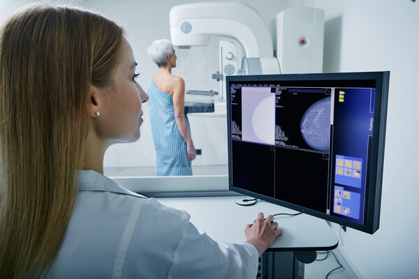 A mammogram technicial looking at the scans of a mammogram with patient in the background.