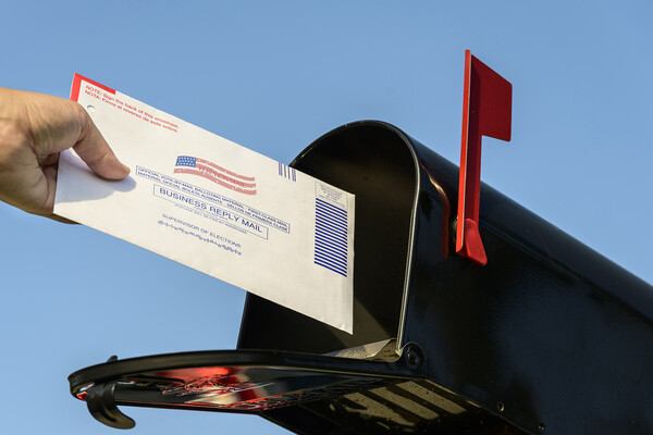 A hand putting a mail-in ballot into a mailbox.