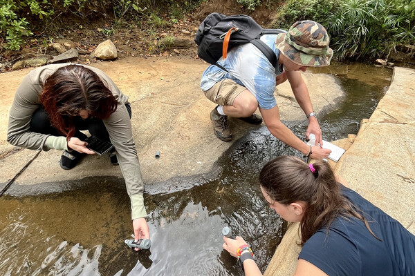 Three people test water below a sand dam.