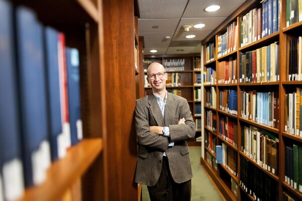 Mendel Kranz leaning against bookshelves in a library setting