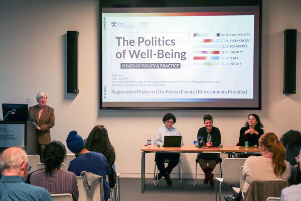 Three people sitting at front of room with slideshow behind them.