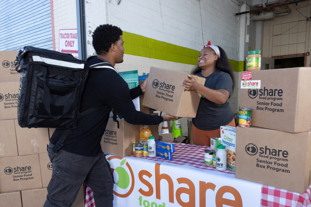 A volunteer with Penn Medicine SHARE Food Program hands a box of food to a bike courier.
