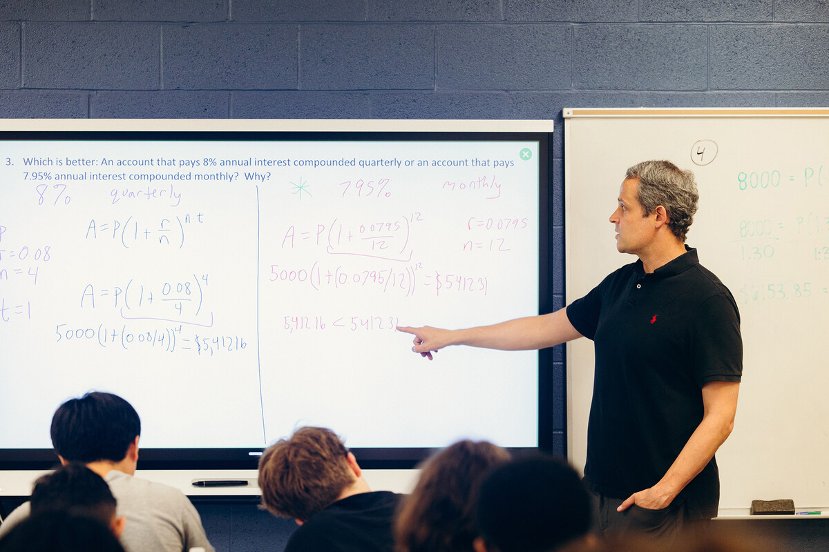 A teacher pointing ot a whiteboard in a high school classroom.