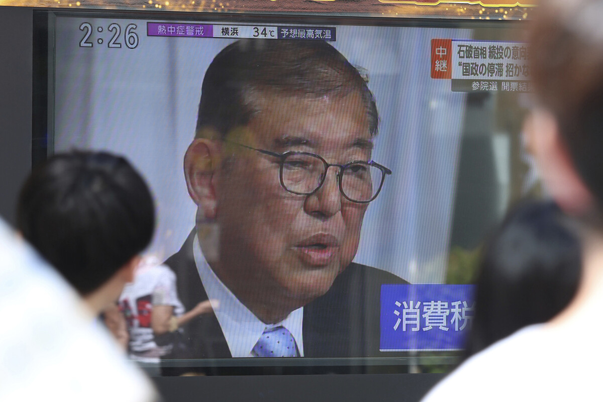 A man is seen on a television screen, framed by the heads of people watching.