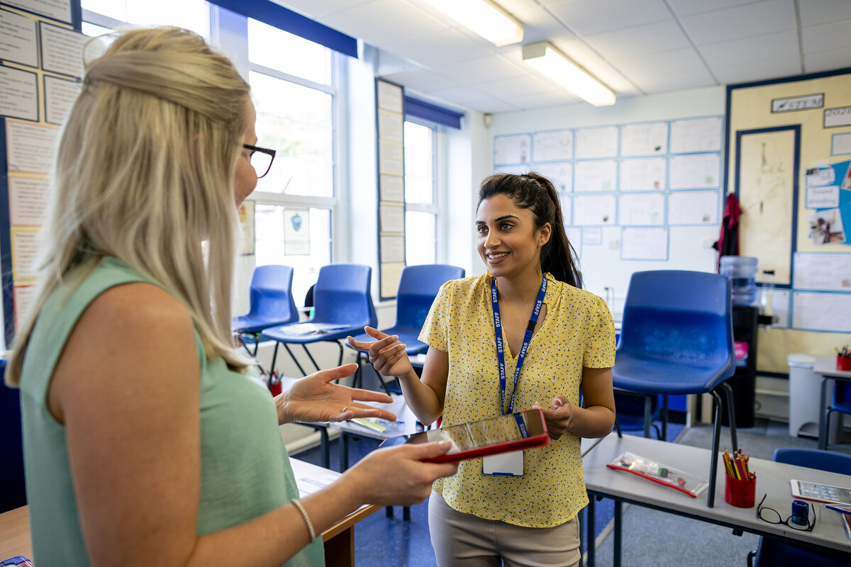 Two teachers having a discussion in a classroom.