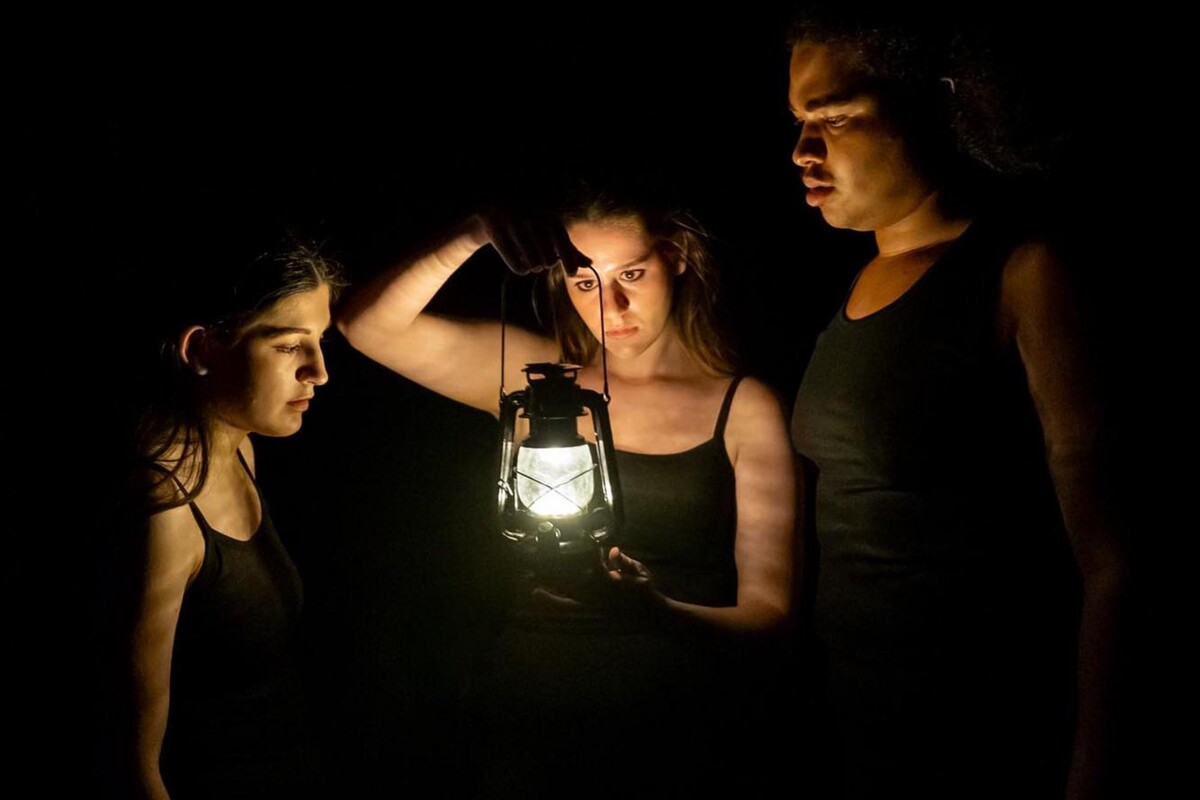 Anya Rothman, Pandora Schoen, and Elliot Ross-Dick looking at an oil lamp in the dark.