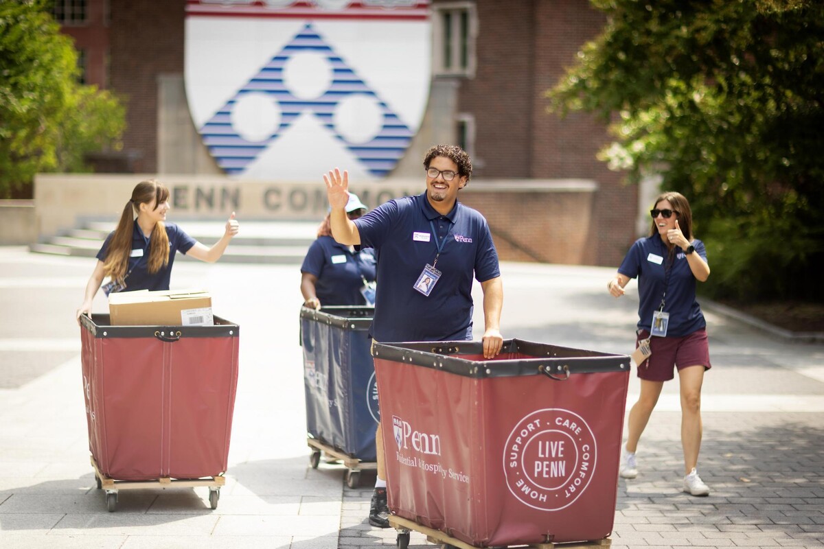 Four students walking through Penn Commons, three pushing Move-In carts.