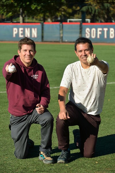 Researchers Douglas Jerolmack and Paulo Arratia kneel on a field at Penn, each holding a baseball